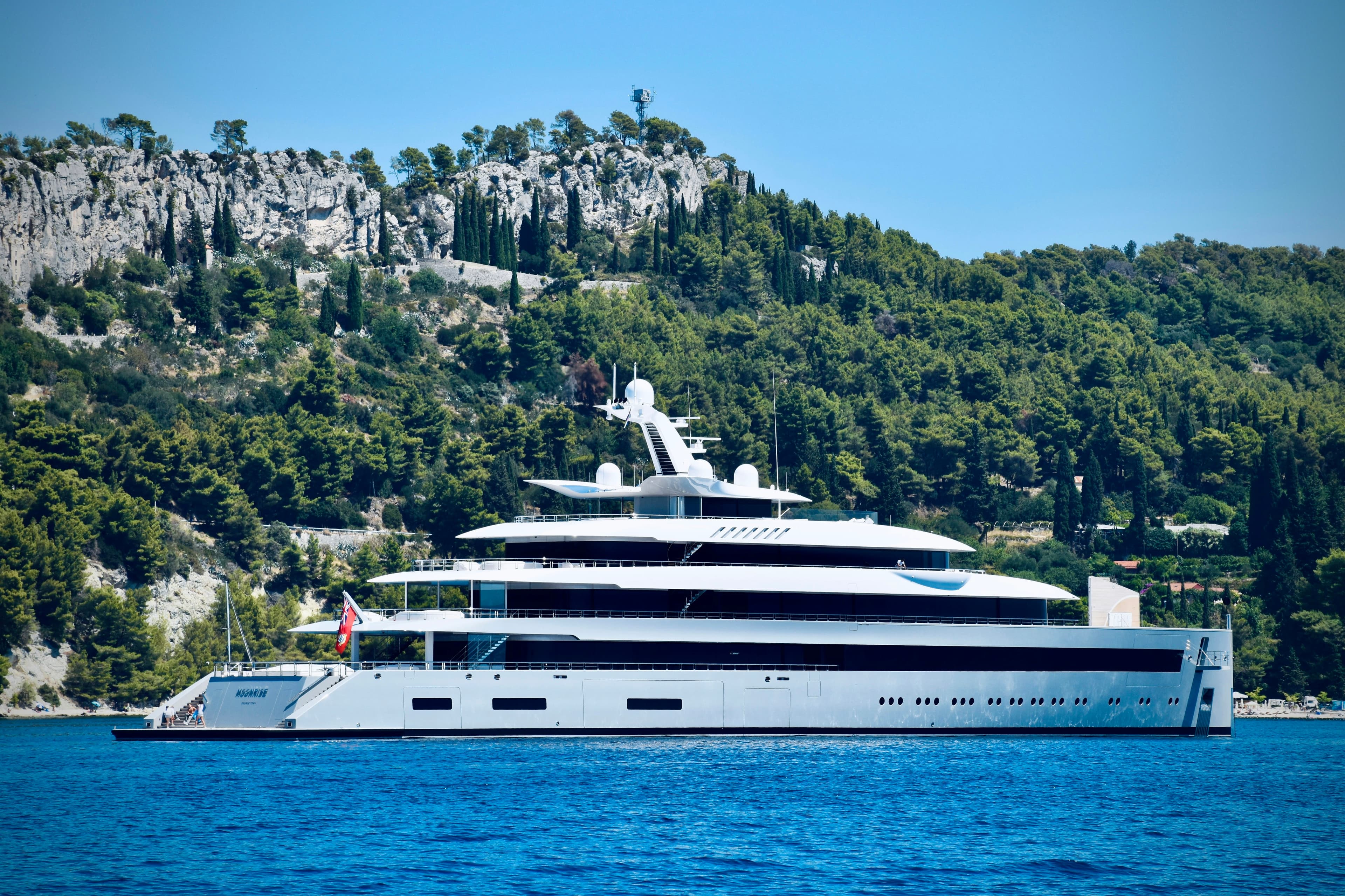 A white superyacht at anchor beside a wooded coastline